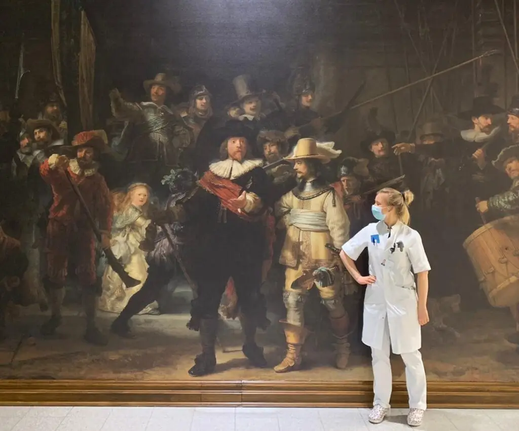 Vrouw in een witte jas staat voor het schilderij De Nachtwacht