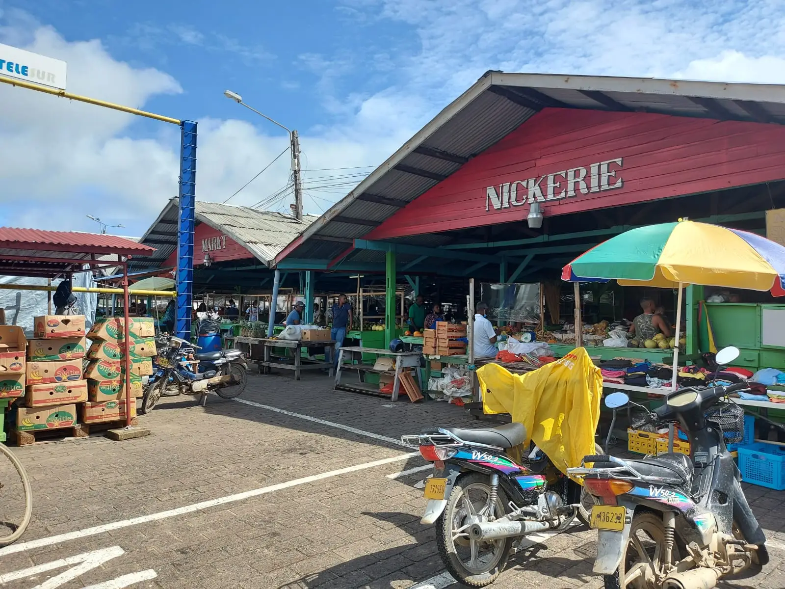 Overdekte markt met het bord ‘Nickerie’ en bromfietsen ervoor