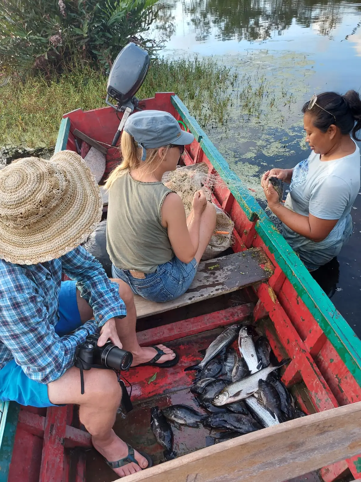Drie mensen in een smalle rode boot, met vis op de bodem