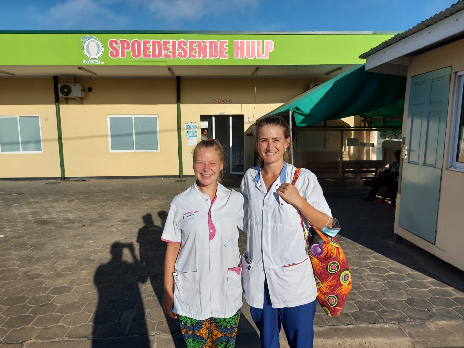 Twee vrouwen in witte jassen voor een gebouw met het bord ‘Spoedeisende hulp’