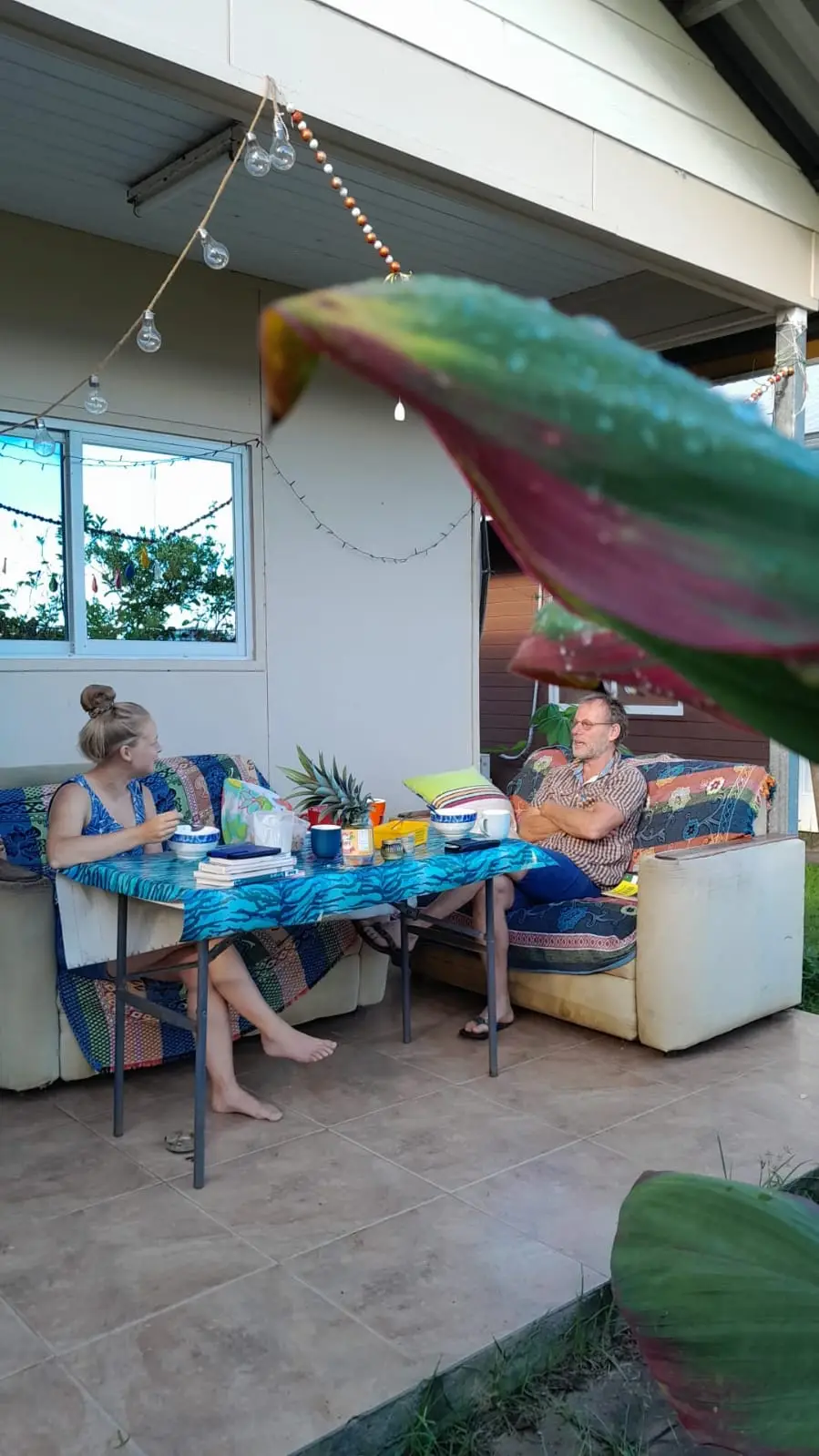 Mensen zitten aan tafel op een open veranda met een grote groene papegaai erboven