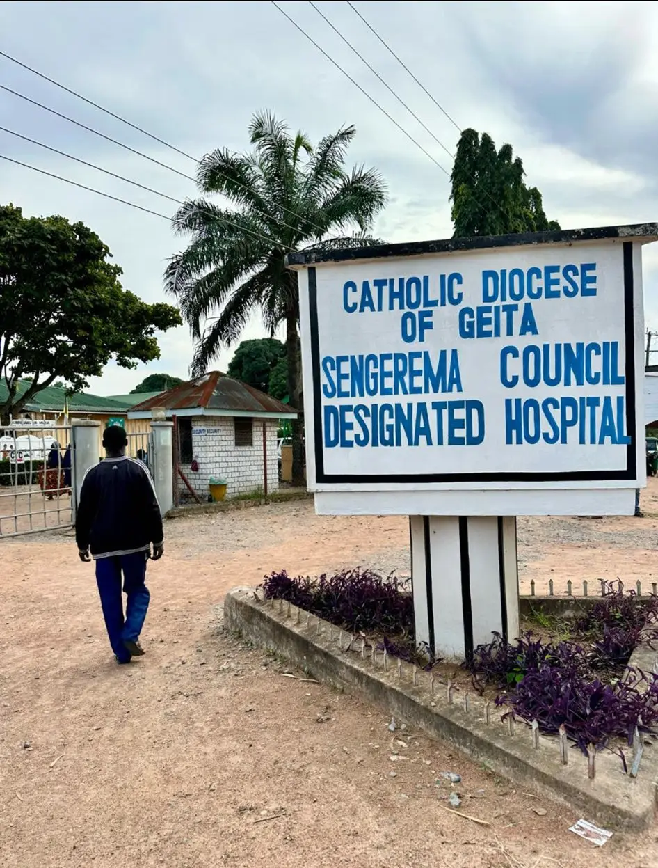 Man loopt over een zandpad langs het bord ‘Sengerema Council Designated Hospital’