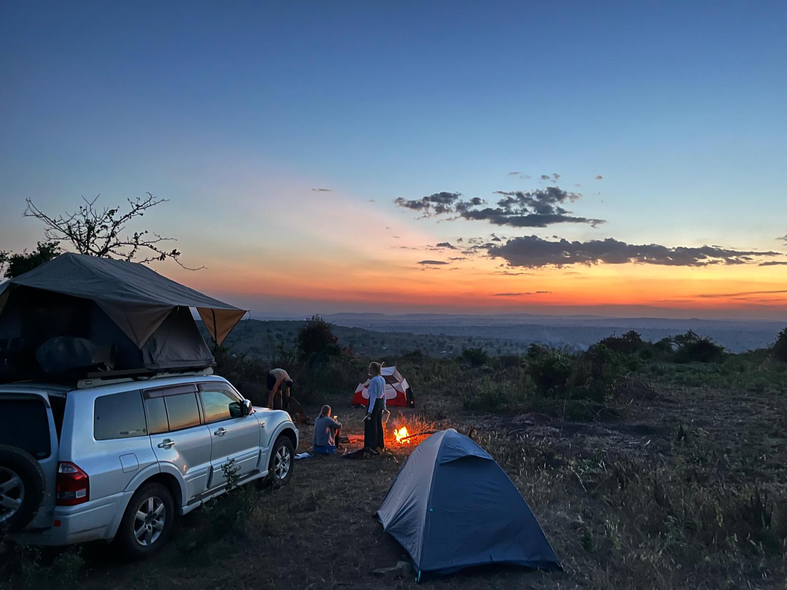 Auto met daktent en een koepeltent op een heuvel bij zonsondergang