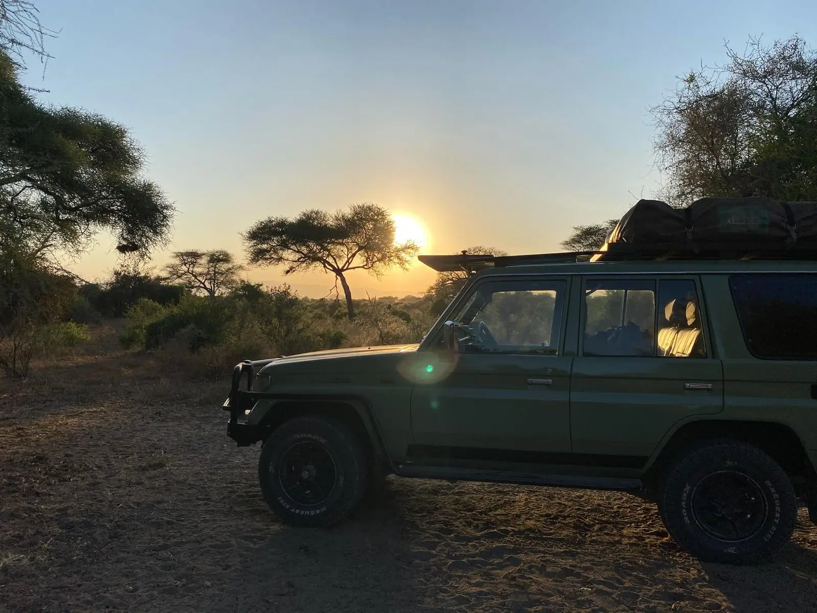 Groene jeep bij zonsondergang tussen acaciabomen