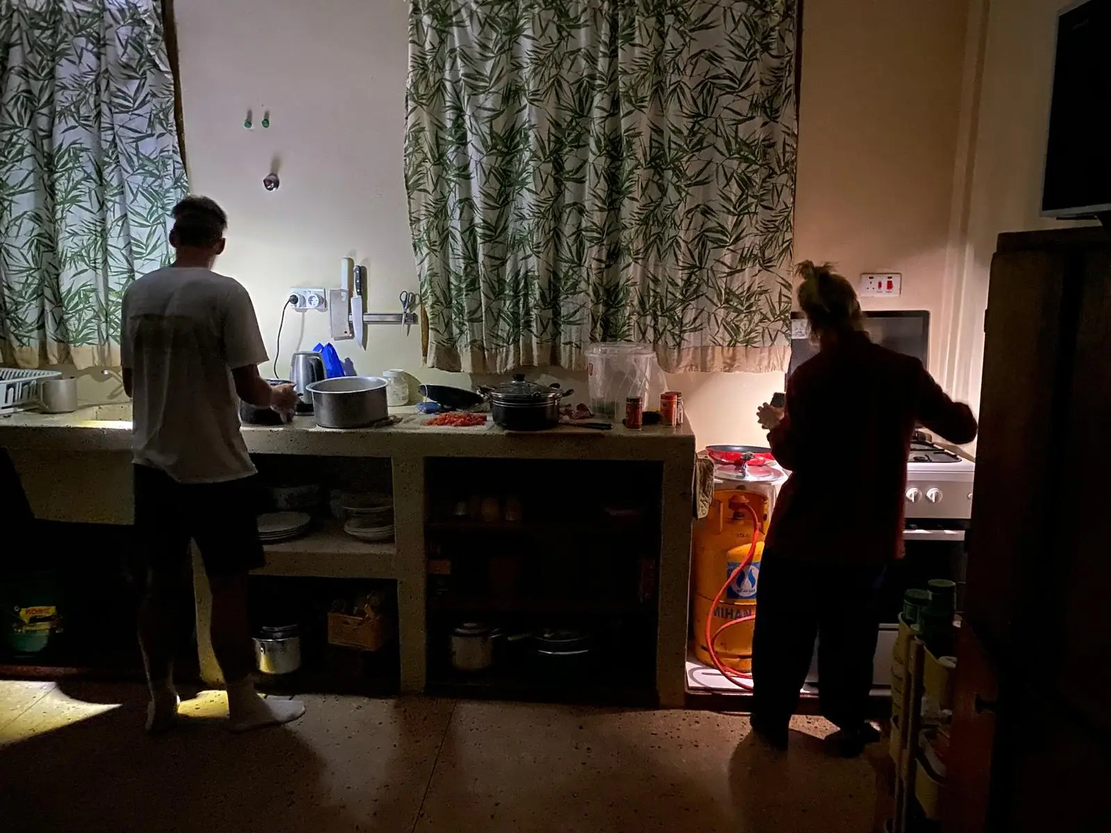Twee mensen staan in een keuken, een bij het aanrecht en een bij het gordijn