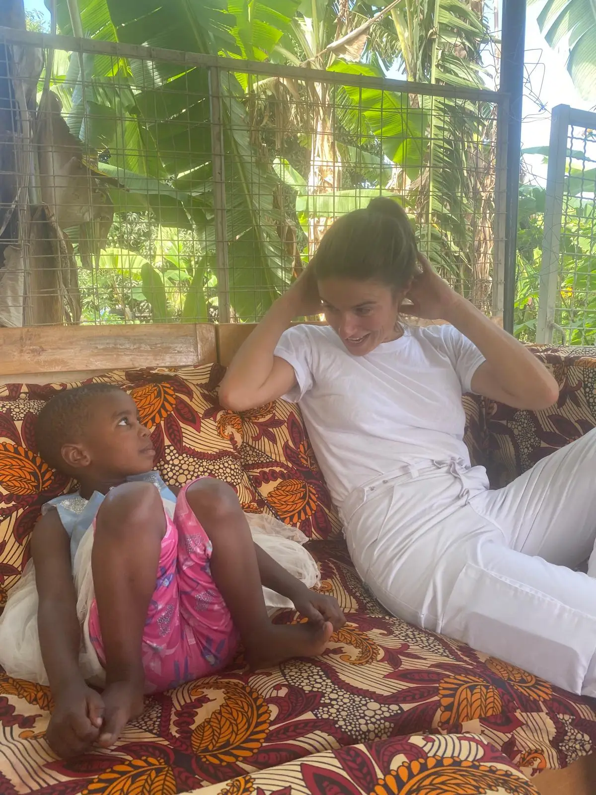 Kind en vrouw zitten ontspannen op kleurige stof onder bananenbladeren