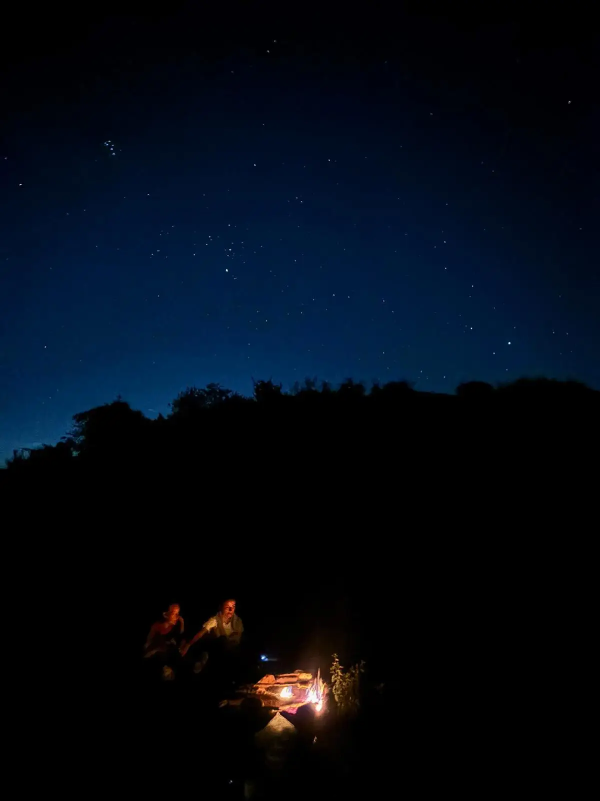 Sterrenhemel in de nacht met in de verte een klein kampvuur