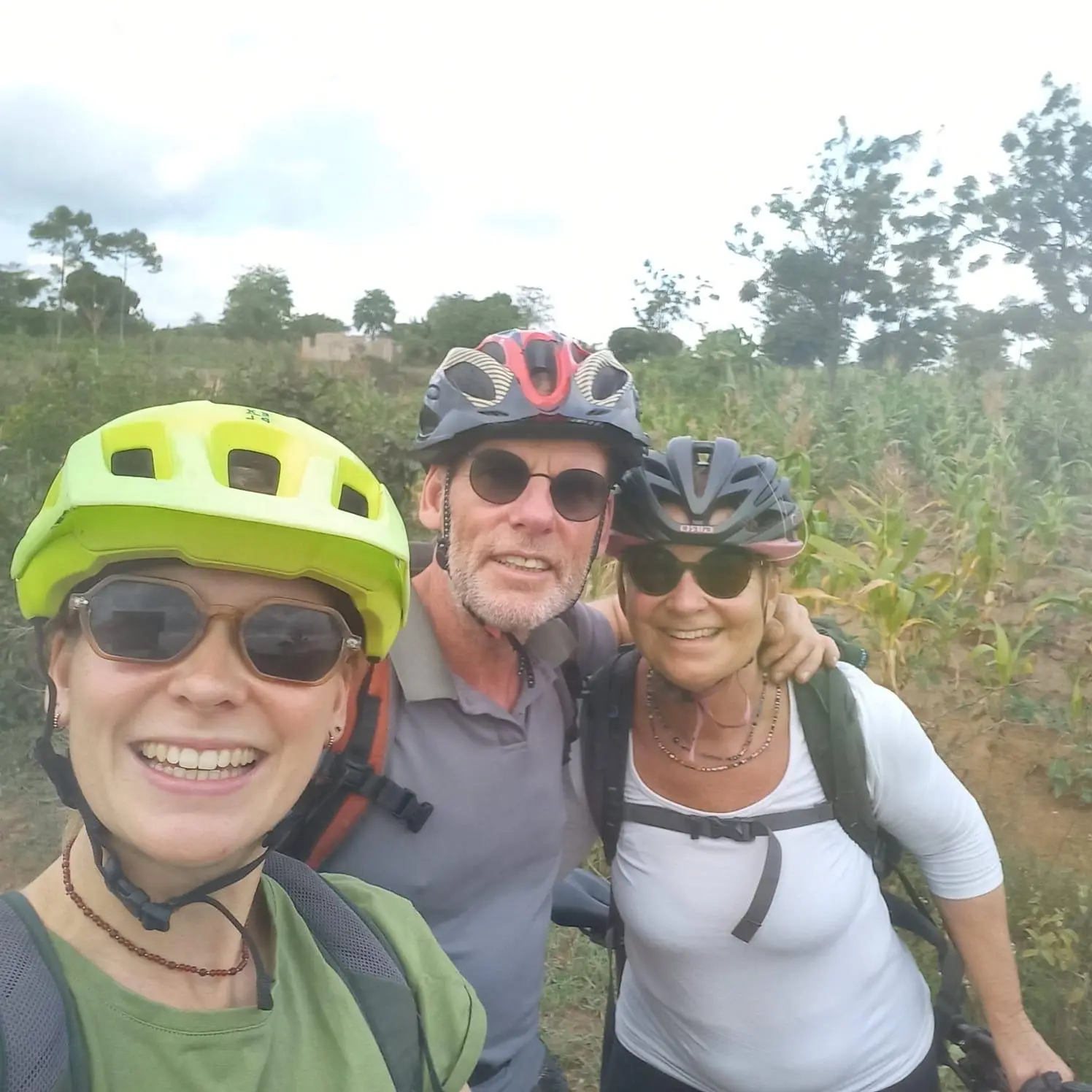 Selfie van drie mensen met fietshelmen en zonnebrillen in het groen