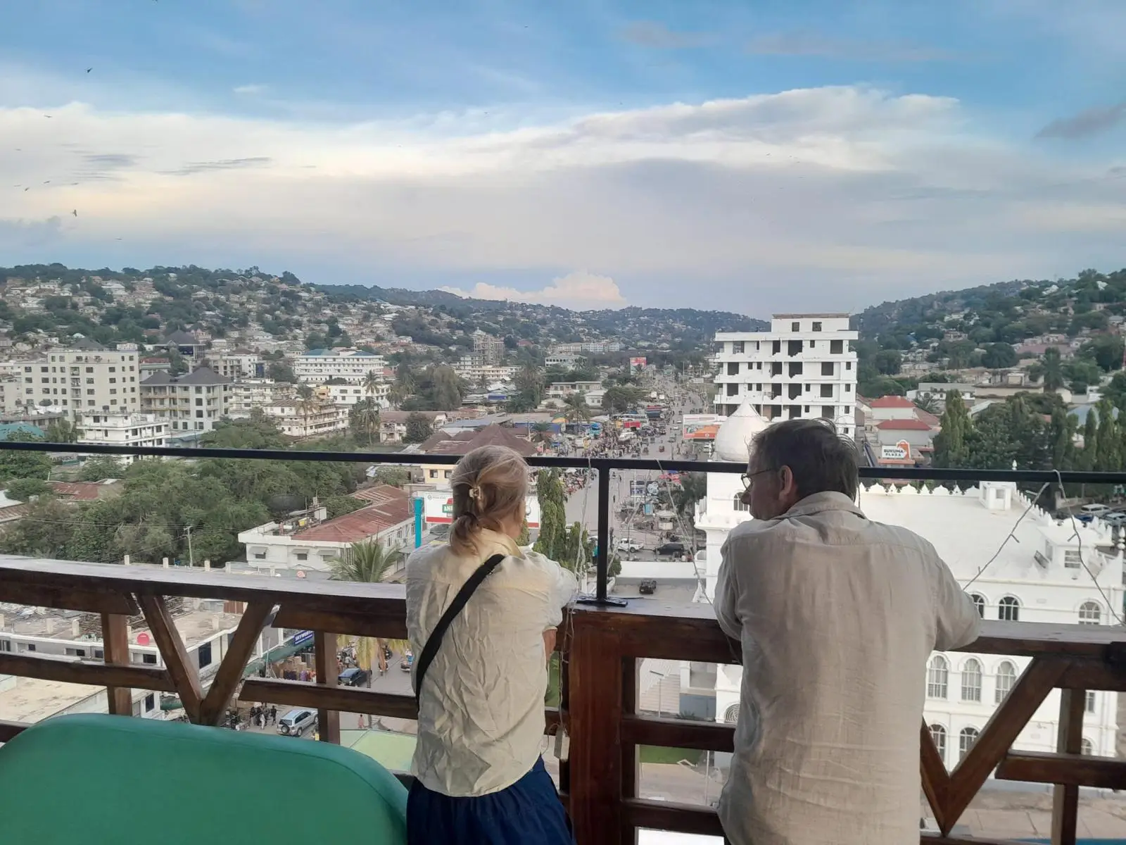 Twee mensen kijken vanaf een balkon uit over de daken van een stad in de heuvels