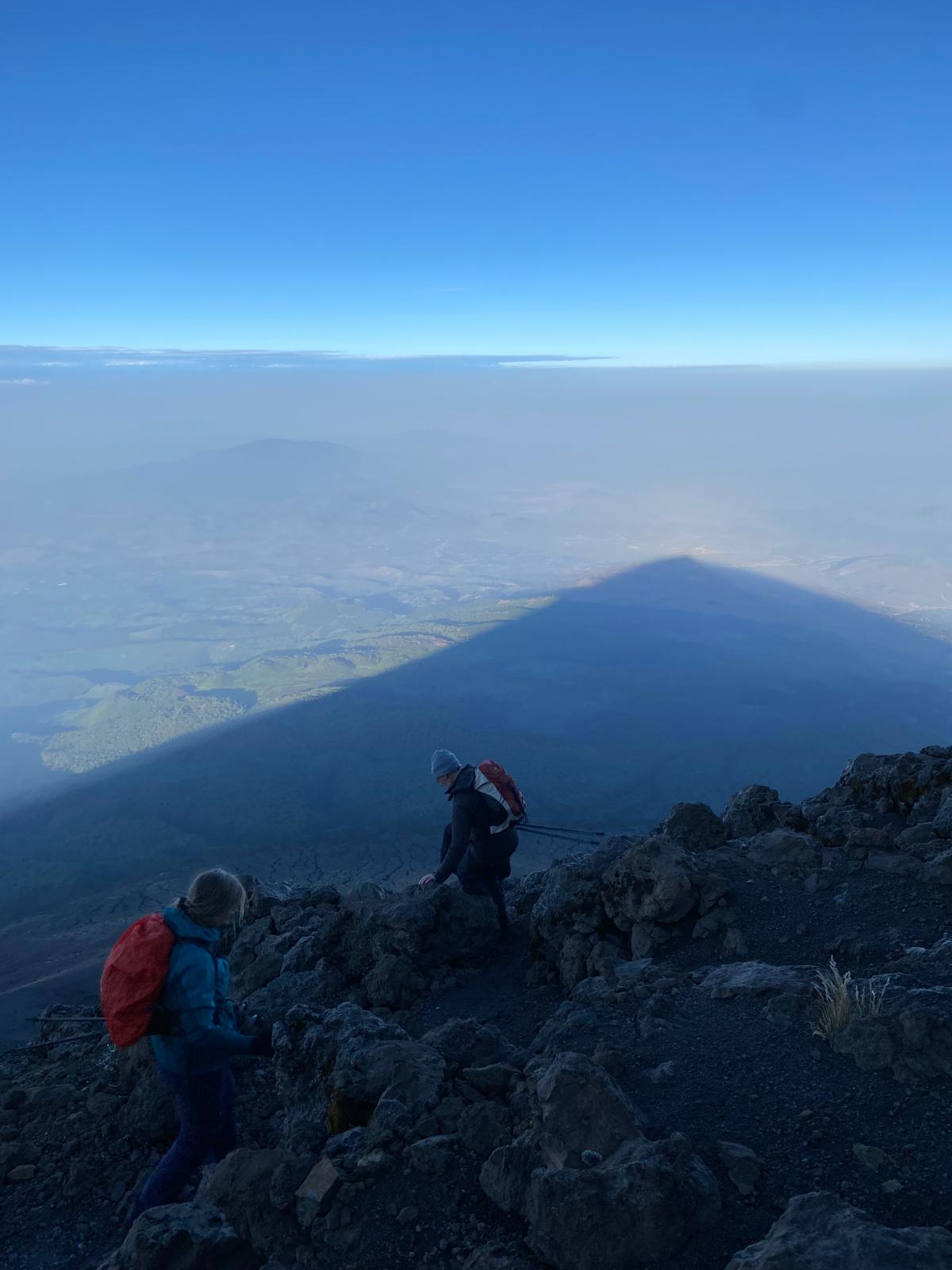 Schaduw van de berg over de wolken, met twee klimmers op de rotsen