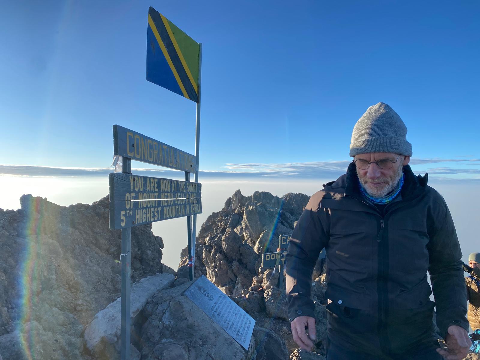 Man met muts en winterjas bij het topbord en de Tanzaniaanse vlag
