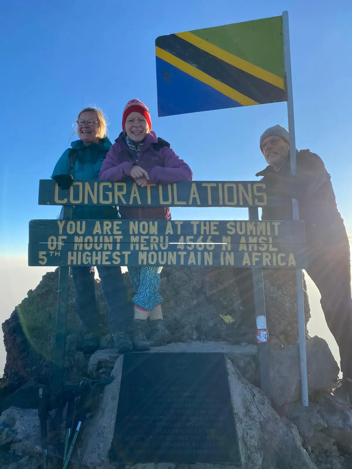 Drie mensen staan bij het topbord naast de Tanzaniaanse vlag