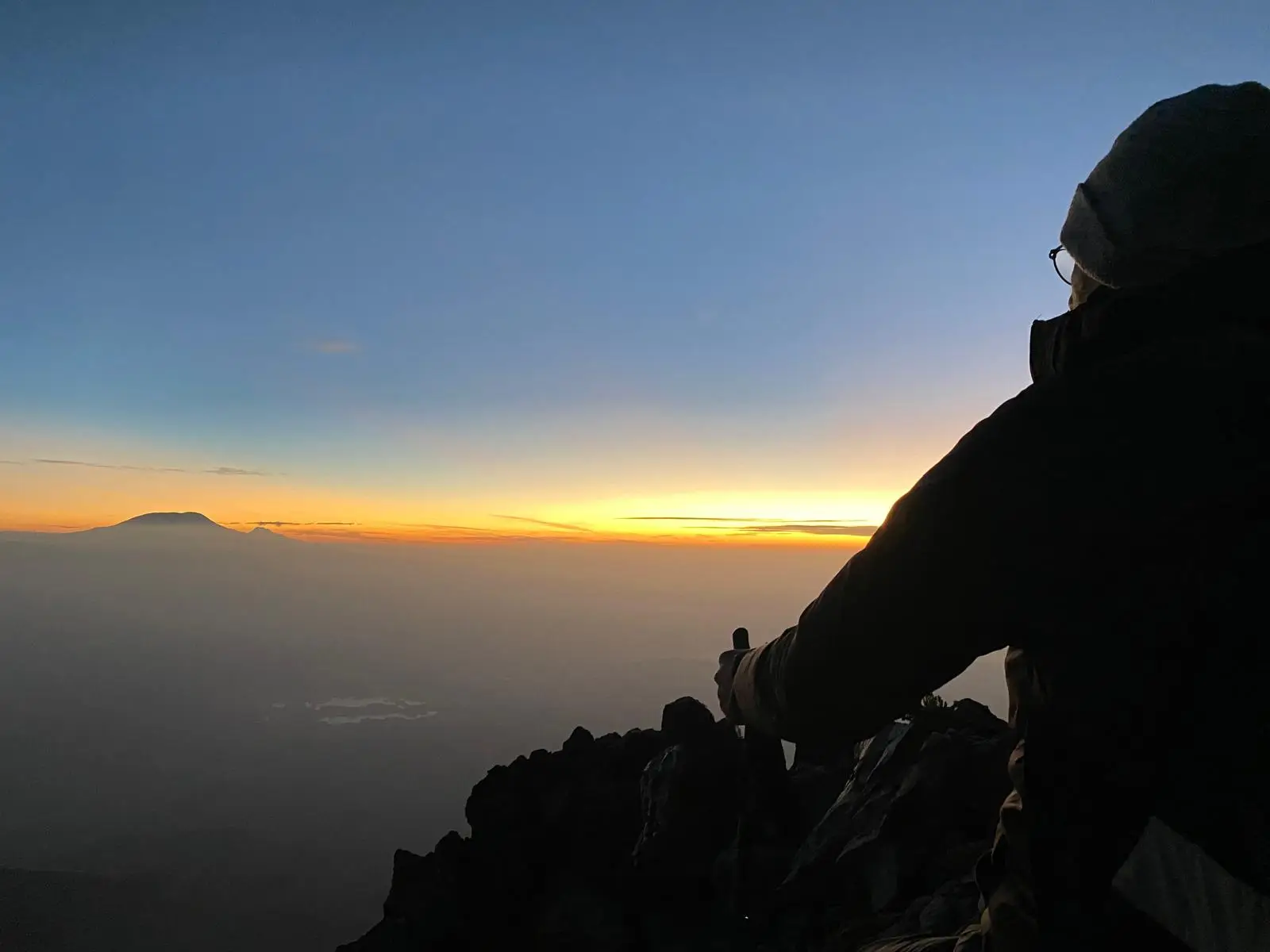 Silhouet van een berg en een klimmer tegen een oranje horizon
